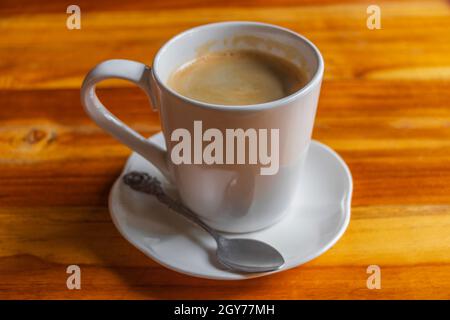 Schwarze Kaffeecrema in einer weißen Tasse mit Löffel auf einem Holztisch in Luang Prabang Laos. Stockfoto