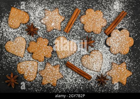 Nahaufnahme Herz und Stern geformt Weihnachten Lebkuchen Cookies mit Zimt und Sternanis Gewürze auf schwarzem Schiefer Hintergrund mit Weißer Puderzucker i Stockfoto