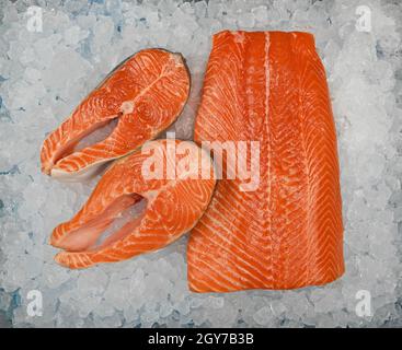Nahaufnahme von frischem Roh-Lachsfischfilet und Steaks vor dem Hintergrund von zerkleinertem Eis auf der Verkaufsfläche, erhöhte Ansicht von oben, direkt darüber Stockfoto
