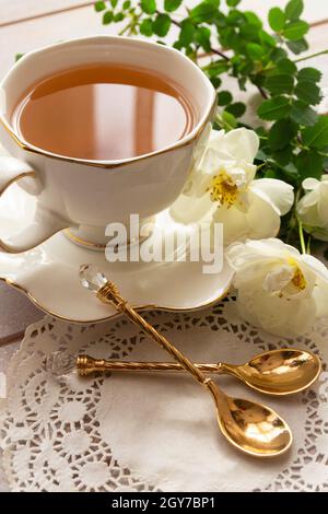 Wunderschönes Bouquet von frischen Rosen in alter antiker Fayence, Keramik, Porzellanbecher mit goldenem auf runder gealterter Platte, porzellanbecher mit goldenen Löffeln. Stockfoto