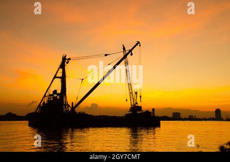 Silhouette Baustelle schweben über Fluss mit Reflexion auf den Sonnenuntergang. Bau Konzept. Stockfoto