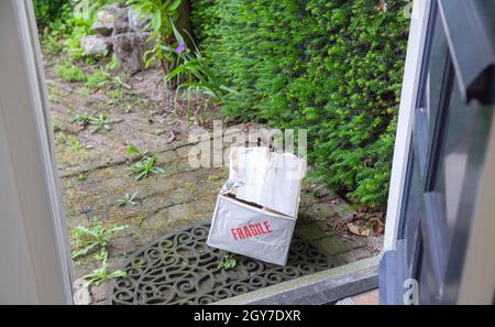 Beschädigter Lieferkarton an der Haustür eines Hauses, zerbrechliches Paket mit Beulen, schlechtes Lieferkonzept in der Nähe Stockfoto