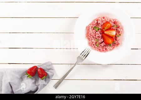 Risotto mit Erdbeerfrüchten serviert in einem weißen Gericht auf einem Holztisch. Flach liegend mit Kopierraum. Italienische Gourmetküche. Selektiver Fokus. Stockfoto