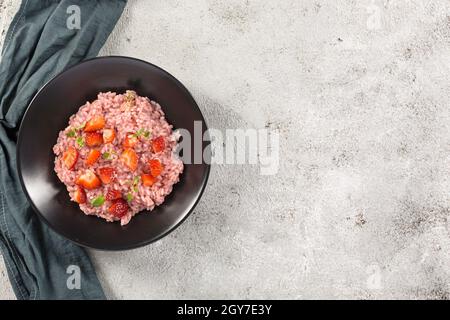 Risotto mit Erdbeerfrüchten serviert in einem schwarzen Gericht auf einem grauen Steintisch. Flach liegend mit Kopierraum. Italienische Gourmetküche. Selektiver Fokus. Stockfoto