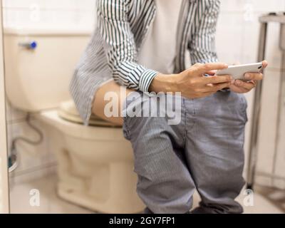 Der Mann hat Durchfall in der Toilette und nutzt das Mobiltelefon horizontal, um Handyspiele zu spielen/Videos auf dem Mobiltelefon anzusehen Stockfoto