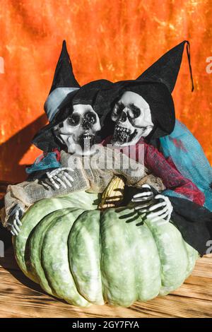 Zwei menschliche Skelette, Freunde, Geister in Lumpen und Hüten, ergriffen gierig großen Kürbis mit knöchernen Händen. Helles Licht, orangefarbener Hintergrund. Halloween-Konzept Stockfoto