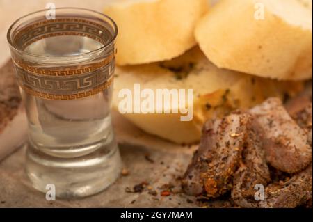 Hausgemachter Speck in Scheiben mit Pfeffer, Brotscheiben und einem Glas hausgemachten Moonshine, Nahaufnahme, selektiver Fokus Stockfoto