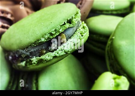 Viele bunte Makronen Kekse ungeordnet angeordnet. Im Vordergrund die grünen mit Pistazien-Geschmack. Gebackener Kuchen mit verschiedenen Farben Stockfoto