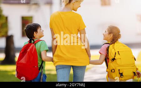 Mutter, die mit Sohn und Tochter auf dem Schulhof läuft. Mutter begleitet die Kinder zur Schule. Konzept von Familienbeziehungen und Studium. Stockfoto