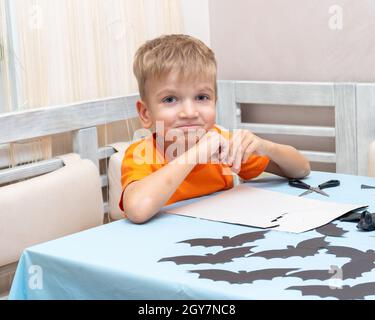 Ein Junge zeichnet und schneidet zu Hause eine Halloween-Dekoration aus schwarzem Papier. DIY Handwerk Dekorationen. Kind macht schwarze Fledermäuse aus Papier, Origami Stockfoto