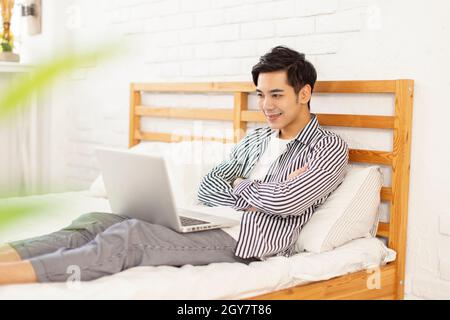 Hübscher junger Mann, der im Bett liegt und mit einem Laptop Filme guckt Stockfoto