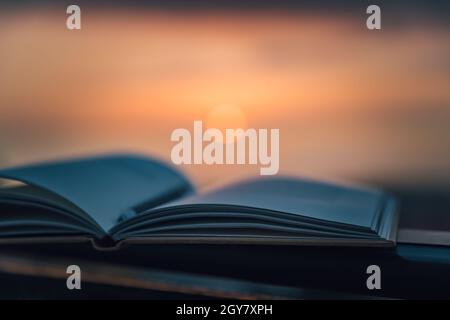 Warmer gemütlicher Abend mit einem interessanten Buch im Freien. Mildes Licht Bei Sonnenuntergang. Stift, um die wichtigsten Dinge zu markieren. Ruhige Angenehme Zeitvertreib. Stockfoto