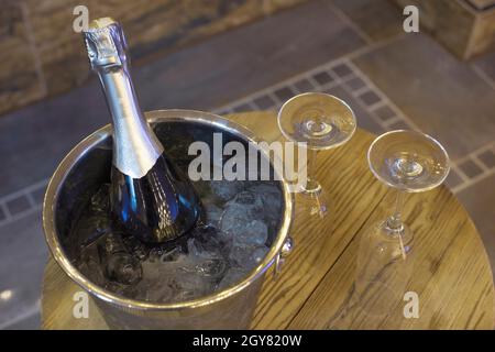 Champagner-Flasche im Kühler, Eimer mit Eis und zwei Sektgläser auf Holztisch. Romantisches Abendessen und Party-Konzept aus der Nähe Stockfoto