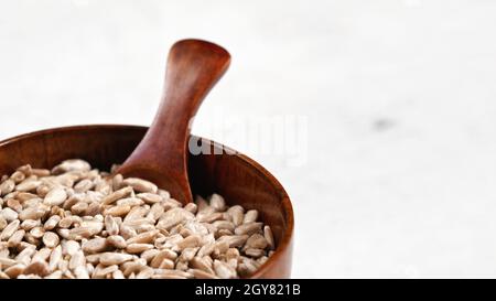 Geschälte Sonnenblumenkerne in kleiner Holzschale oder Tasse mit Löffel auf weißem Brett, Platz für Text rechts. Stockfoto