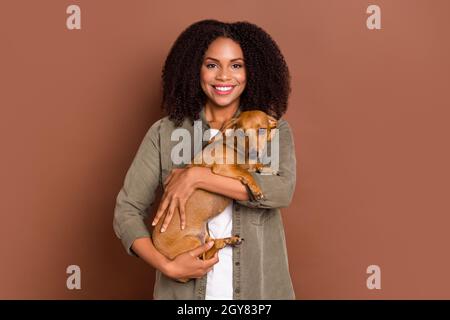 Foto von lustigen jungen Brünette Dame halten Hund tragen Hemd isoliert auf braunem Hintergrund Stockfoto