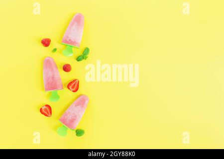 Flaches Lay mit fruchtigem rosa gefrorenem Sorbet Eis auf grüner Plastikstick Sammlung mit Schnitten von Erdbeere, Minzblätter auf gelbem Hintergrund. Gefroren Stockfoto