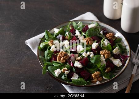 Rüben- oder Rote Beete-Salat mit frischer Rucola, Weichkäse und Walnüssen auf dem Teller, Dressing und Gewürzen auf dunklem Holzhintergrund, Kopierraum, Draufsicht/ Stockfoto