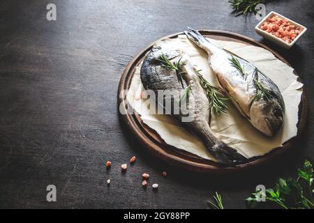 Frischer, roher dorado-Fisch auf einem Holzbrett mit rosafarbenem himalaya-Salz, rosa Pfefferkörnern und Rosmarin Stockfoto