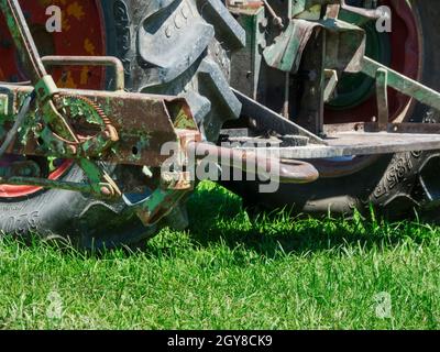 Detailansicht einer veralteten, rostigen und verbogenen Anhängerkupplung an einem Traktor vor einer rauen Reifenlauffläche auf einem Rasen Stockfoto