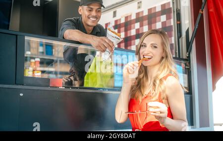 Eine wunderschöne Frau, die bei einem Food Truck Pommes bestellte und einen ersten Bissen nahm Stockfoto