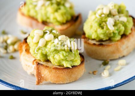 Pürierte Avocado auf geröstetem Baguette-Brot mit Bohnensprossen. Gesunde vegane Vorspeise oder Snack Stockfoto