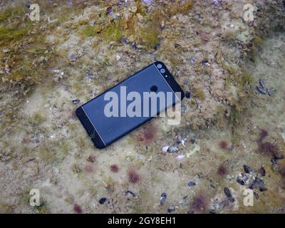 Smartphone unter Wasser. Beschädigtes Smartphone ertrank im Meer. Stockfoto