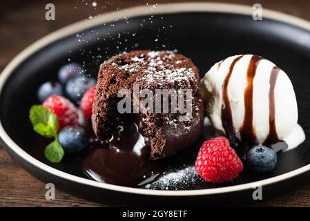 Schokoladenkuchen mit Fondant, geschmolzener Lavakuchen mit Eisportionierer und frischen Beeren auf dem Teller Stockfoto