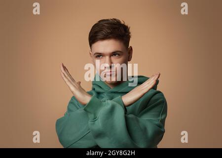 Junger gutaussehender Kerl im Sweatshirt zeigt Stop-Geste isoliert auf braunem Hintergrund. Menschliche Emotionen, Gesichtsausdrücke Stockfoto