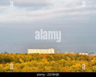 Blick über den farbenfrohen Stadtpark und das große Hochhaus am Horizont am sonnigen Herbsttag Stockfoto