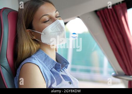 Nahaufnahme der jungen schönen Frau mit medizinischen Maske FFP2 KN95 schlafen im Bus sitzen. Busspassagier, der sicher auf einem Sitz sitzt und einen Schlafplatz hat Stockfoto