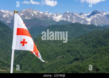 Die Flagge Georgiens winkt auf dem Hintergrund der Berge und des blauen Himmels. Georgische Nationalflagge. Selektiver Fokus Stockfoto