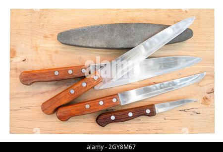 Draufsicht auf gebrauchte Küchenmesser und Schleifstein auf Holzbrett Stockfoto