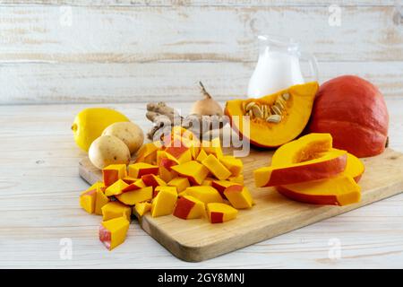 Gehackter roter Kuri-Kürbis und Zutaten für ein vegetarisches Thanksgiving- oder Halloween-Menü mit Kokosmilch, Ingwer, Kartoffeln und Zitrone auf einem leichten Waldholz Stockfoto
