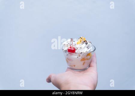 Tasse Pfirsiche und Creme auf Handfläche mit hellblauem Hintergrund Stockfoto