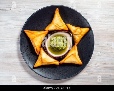 Draufsicht auf peruanische Empanadas (gebratener Umsatz gefüllt mit Fleisch) mit grüner Chimichurri-Sauce auf Teller auf Holzbrett Stockfoto