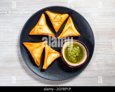 Portion peruanische Empanadas (gebratener Umsatz gefüllt mit Fleisch) mit grüner Chimichurri-Sauce auf dem Teller auf Holzbrett Stockfoto
