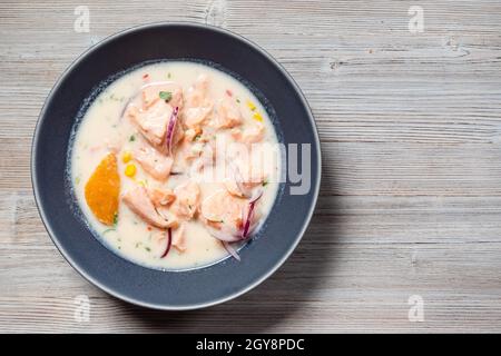 Draufsicht auf peruanischen Lachs-Ceviche in Leche de Tigre-Sauce mit Süßkartoffeln und Mais in Schale auf grauem Holztisch mit Copyspace Stockfoto