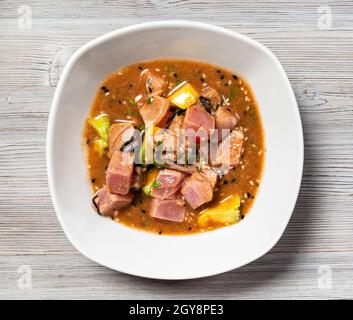 peruanischer Thunfisch-Ceviche in Tamarindensauce mit Avocado-Stücken und Algen in einer Schüssel auf grauem Holzbrett Stockfoto