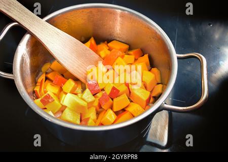 In Scheiben geschnittener roter Kürbis oder Hokkaido-Kürbis in einem Edelstahltopf auf einem schwarzen Induktionsherd, der ein Gemüserezept für Suppe oder Püree in der Aue kocht Stockfoto