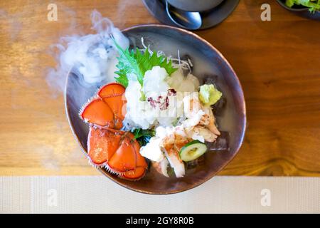 Live Canadian Lobster Sashimi auf brauner Keramikplatte mit einem Rauch aus trockenem Eis. Serviert zwei Arten frisch und gekocht dekorieren mit frischen Wasabi, geschreddert ra Stockfoto