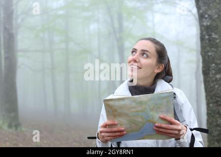 Glücklicher Wanderer mit einer Papierkarte, der an einem nebligen Tag in der Natur auf die Seite schaut Stockfoto