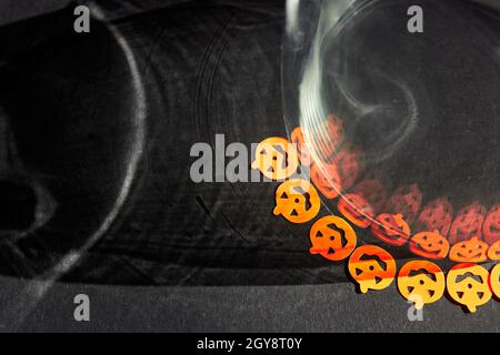 Leuchtend orange kleine Kürbisaufkleber werden von gruseligen Schatten in einem Glasglas reflektiert. Leuchtend orange Halloween Kürbisse auf einem dunkelgrauen Hintergrund. Stockfoto