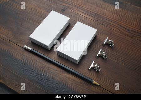 Leere Visitenkarten, Bleistift und Büroklammern auf Holzhintergrund. Schreibwaren-Modell. Stockfoto