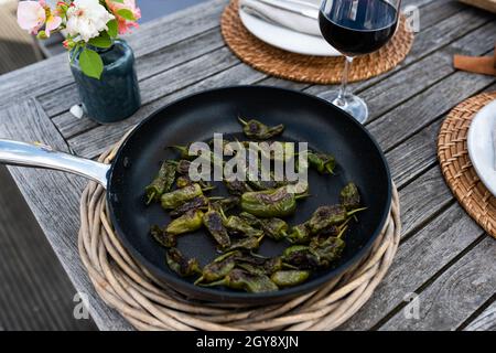 Frisch gebratene grüne Pimientos in einer Pfanne auf einem Holztisch. Pimientos de padron. Nahaufnahme mit kurzer Schärfentiefe. Stockfoto