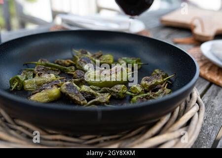 Frisch gebratene grüne Pimientos in der Pfanne. Pimientos de padron. Nahaufnahme mit kurzer Schärfentiefe. Stockfoto