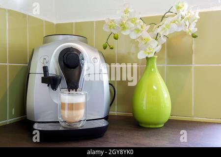Kaffeemaschine mit einem Latte Macchiato in gemütlichen dekorativen Haus mit grünen Wand und Blumen. Hausgemachter Kaffee stilvoll Stockfoto