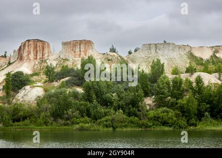 Wunderschöne Naturlandschaft. Weiße Kreidefelsen, Baumdickichte, ein wolkig bewölkter Himmel, ein ruhiger See am Fuße des Berges. Kalksteinbruch. Berg Stockfoto