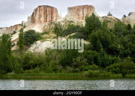 Wunderschöne Naturlandschaft. Weiße Kreidefelsen, Baumdickichte, ein wolkig bewölkter Himmel, ein ruhiger See am Fuße des Berges. Kalksteinbruch. Berg Stockfoto