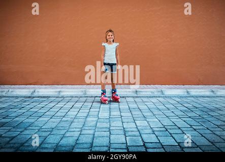 Nette glückliche kleine Mädchen Rollerblading im Hof. Viel Spaß Im Freien. Perfekte Sommerrekreation. Gesundes Sportliches Sommerurlaube-Konzept. Stockfoto