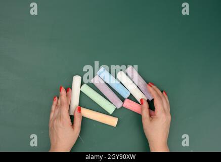 Hand hält ein Stück weiße Kreide auf dem Hintergrund einer leeren grünen Kreidetafel, Präsentationskonzept, zurück zur Schule Stockfoto